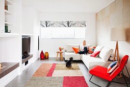 Designer Wohnzimmer mit rotem Schaukel-Sessel neben Couch mit Frau und Hund vor Fenster