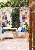 White, rattan outdoor furniture on terrace with terracotta floor and colourful tiles on courtyard wall