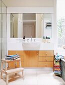 Geräumiger Waschtisch mit Holzfronten, überkragendem Becken und Spiegelfront, daneben Blick aus dem Fenster über der Wanne