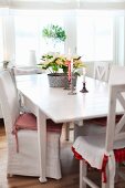 Chairs with white loose cover and kitchen chairs around lit candles & potted plant on table