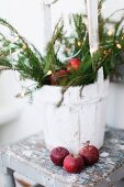 Red apples in front of whitewashed bucket of branches with festive decorations on vintage stool