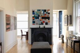 Modern artwork above central open fireplace flanked by open doorways with further artworks and console table; ottoman in foreground