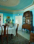 Herrschaftliches Esszimmer hellblau getönt, gedeckter Tisch gegenüber antikem Vitrinenschrank