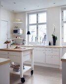 Island counter with drawers on castors in white, country-house kitchen with recessed spotlights in suspended ceiling
