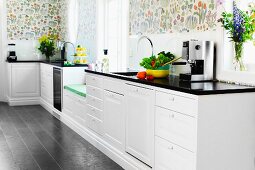 White country-house kitchen with black worksurface below colourful floral wallpaper