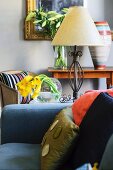 Blue sofa with scatter cushions in front of table lamp and vases of flowers