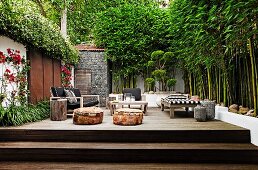 Various terrace furnishings on wooden platform with steps in courtyard with tall bamboo against wall