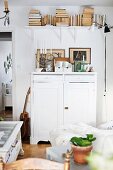 Half-height, white wooden cabinet and books on wall-mounted shelf in rustic living room