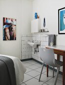 Grey plastic chair at table next to minimalist washing area in corner of bedroom with modern artworks on walls