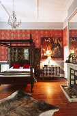 Traditional four-poster bed with turned wooden bedposts and red wallpaper with ornamental pattern in traditional, country-style bedroom