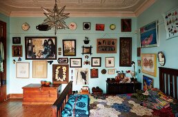 Patchwork quilt on bed and gallery of artworks on turquoise-painted wall in artistic interior