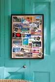 Gerahmte Pinnwand mit verschiedenen Ansichtskarten an türkisfarbener Kassettenverkleidung einer Vintage Veranda