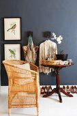 Pale bamboo chair an antique side table against black-painted wall with framed pictures of birds & coat hooks