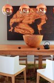 Spherical, copper pendant lamps above wooden bowl on table and chairs with white backrests and arms