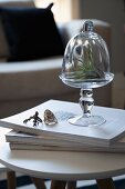 Glasschale mit Glashaube und Fingerringe mit Tiermotiven auf einem Bücherstapel