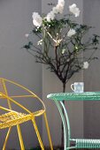 Delicate, vintage wire furniture painted yellow and turquoise in front-garden sunlight; white standard rose against facade in background