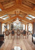 Dining area with long table on elegant parquet floor in front of open-plan kitchen in converted attic storey of modern chalet