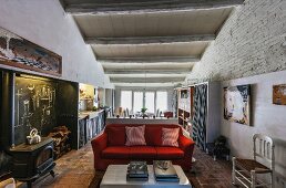 Offener Wohnraum mit rotem Sofa und Holzofen, Wandnische mit Kreidewand, im Hintergrund Küchen mit Essbereich