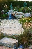 Grosse Steinplatten und Wasserpflanzen im Teich, im Hintergrund Wasserfall
