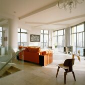 Designer-Stuhl aus Holz und Sofa mit orangefarbener Polsterung im Wohnzimmer einer Penthouse-Wohnung mit raumhohen Fenstern
