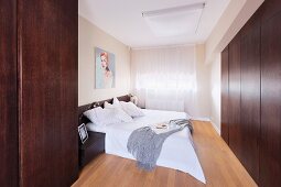 Blick in gediegenes Schlafzimmer mit zeitgenössischem Flair, Doppelbett mit weisser Tagesdecke gegenüber hermetischem Einbauschrank aus dunklem Holz