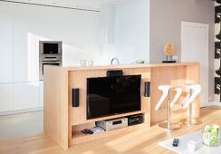 Flatscreen TV mounted on wooden counter and designer bar stools with white seats in open-plan kitchen area