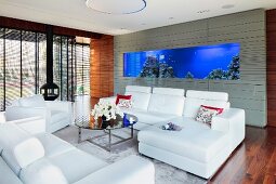 Modern sofa set with white leather covers and coffee table in lounge area; large aquarium incorporated in grey-tiled wall