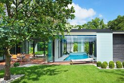 Sunny garden and terrace outside contemporary house with indoor swimming pool