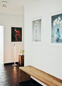 Minimalist wooden bench on slate-style floor covering in contemporary hallway with photos of flowers on walls