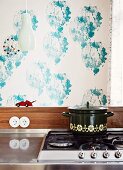 Saucepan on gas hob against wall with blue stencilled pattern on white background