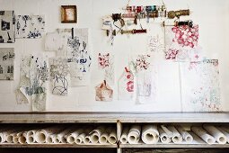 Sketches and reels of yarn hung on wall above shelf of rolled paper