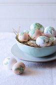 Easter eggs decorated with botanical patterns (decoupage) in nest of straw in bowl