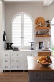 Country-house-style kitchen; custom sideboard with drawers in front of arched window with interior shutters