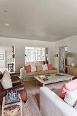 Gemütliches Wohnzimmer mit hellen Hussensofas, pastellfarbenen Kissen und antiken braunen Ledersesseln