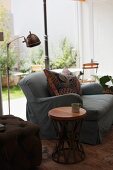 Side table next to sofa and retro standard lamp in front of glass wall in living room