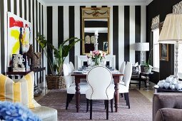 White upholstered chairs around table in dining room with black and white striped wallpaper