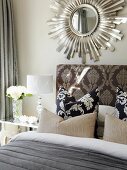 Scatter cushions on bed against upholstered headboard with ornate headboard below mirror with sunburst frame