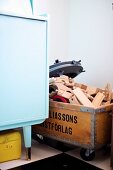 Holzspielzeugteile in recycelter Holzkiste auf Rollen neben Retro Sideboard in Pastellblau
