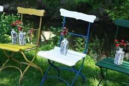 Keramikvasen mit Blumen auf Vintage Gartenstühlen mit bunter Metallgestell