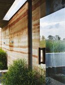 Facade of modern house with rammed-earth structure and reflection of surrounding countryside in glass door