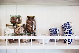 Storage jars and white and blue painted mugs on wall-mounted shelf