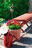 Red arrangement with wooden bench, watering can and planter on gravel garden terrace