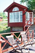 Deckchairs on wooden jetty with red railing in front of Swedish wooden house by the sea