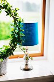Table lamp with blue fabric lampshade next to potted ivy topiary on windowsill