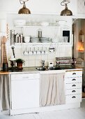 Functional kitchen counter with integrated dishwasher and drawers below cups and crockery on white, wall-mounted shelves