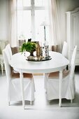 Chairs with white, loose covers around house plant on tray on table in rustic dining room