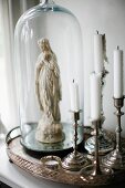 Silver candlesticks next to Madonna figurine under glass covers on silver tray