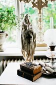 Madonna figurine and antiquarian books next to paraffin lamp in front of window
