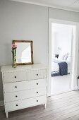 White chest of drawers next to open bedroom door with view of double bed