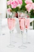 Glasses of pink champagne on table outside with pink roses in background